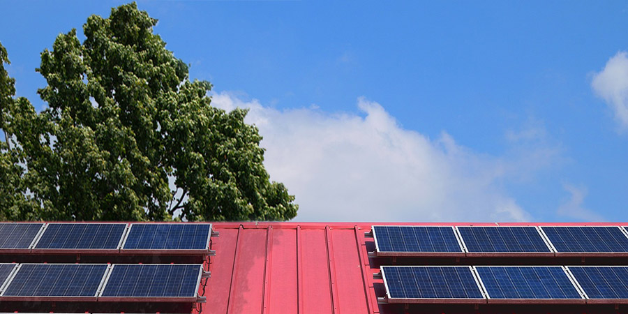 partially shaded solar panels mounted on a red ceramic tile roof, tree and blue sky in the background